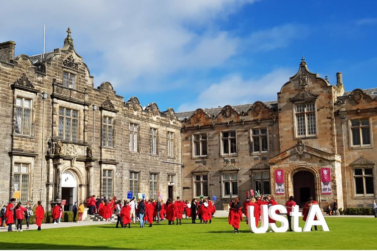 students in red gowns in a grassy area in front of buildings